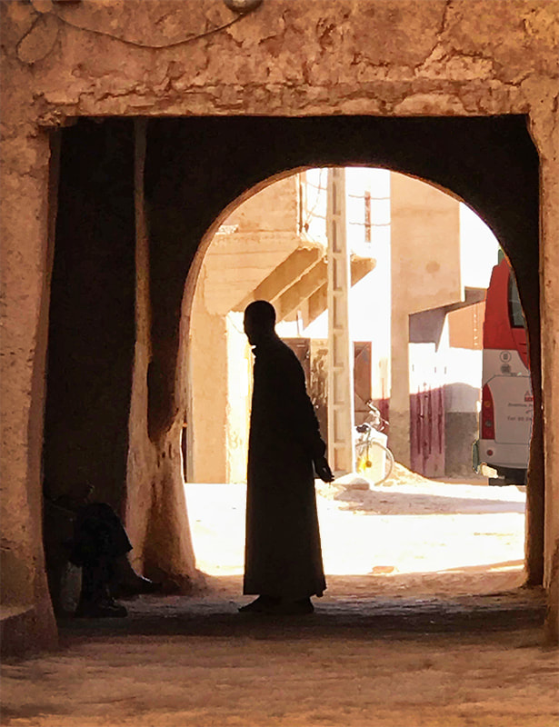 man in djellaba silhouetted in archway in Moroccan desert town.