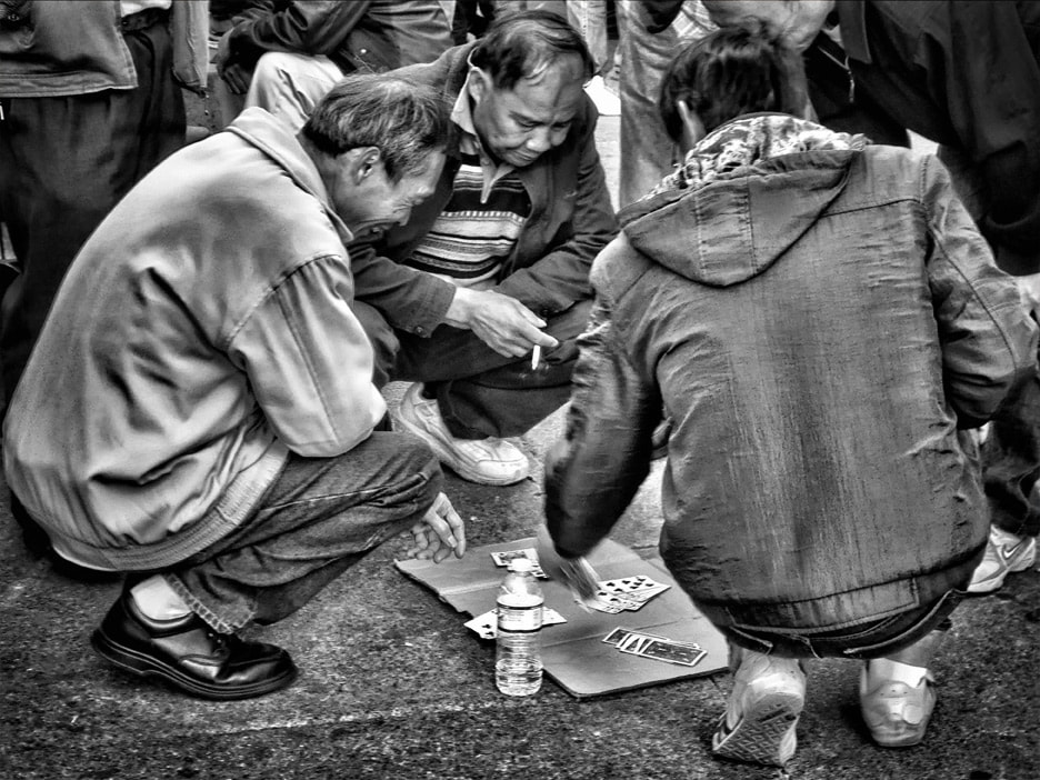 Chinese men playing cards on the ground in the park.  black and white.