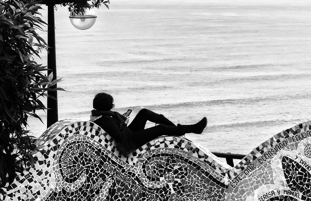 Silhouette of woman on wall by the sea checking her phone. black and white