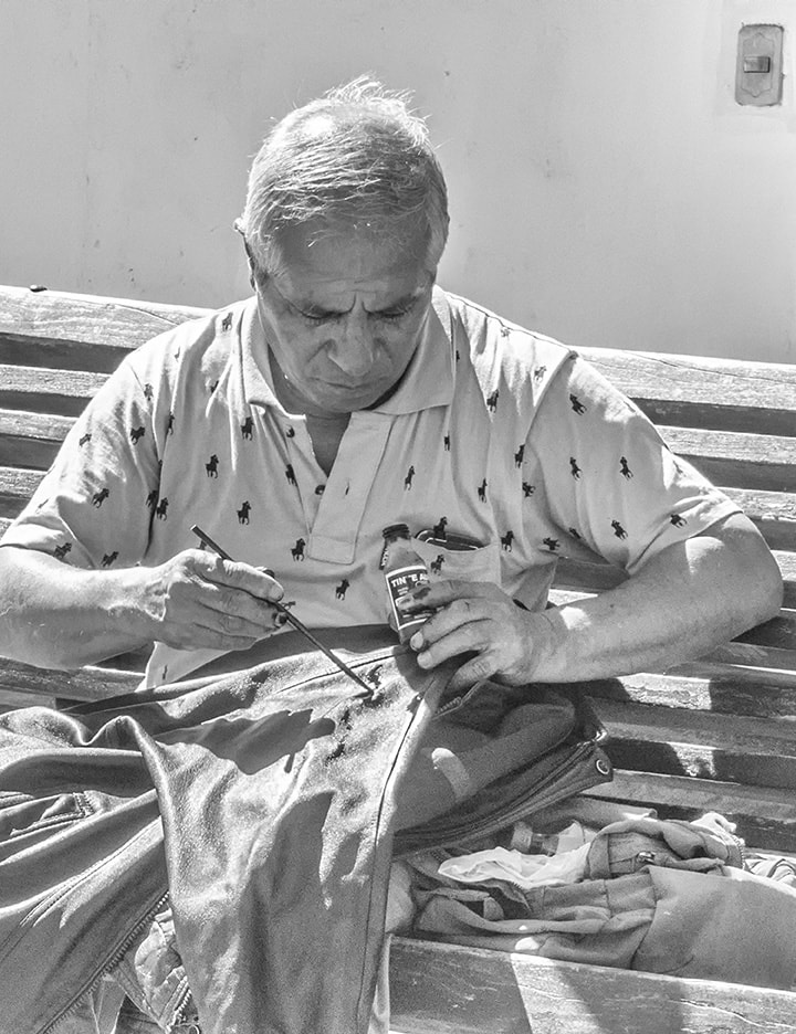 gray haired man on bench mending his jacket