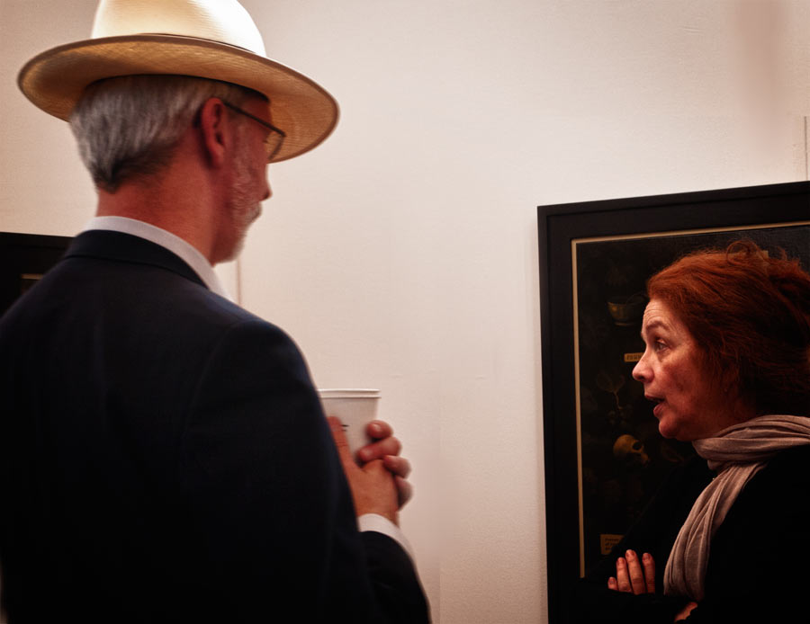 man in straw hat looking at art talking to woman.