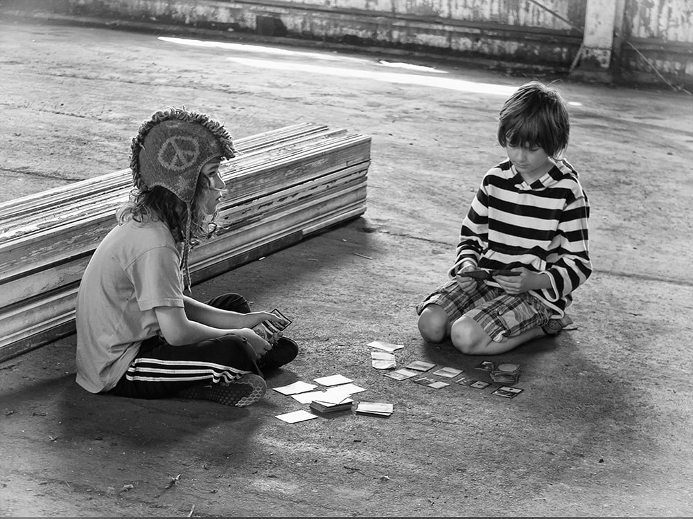 two boys playing cards on floor.  black and white.